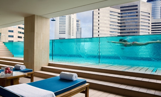 Leisure sun chairs in front of glass tank swimming pool with a child swimming.