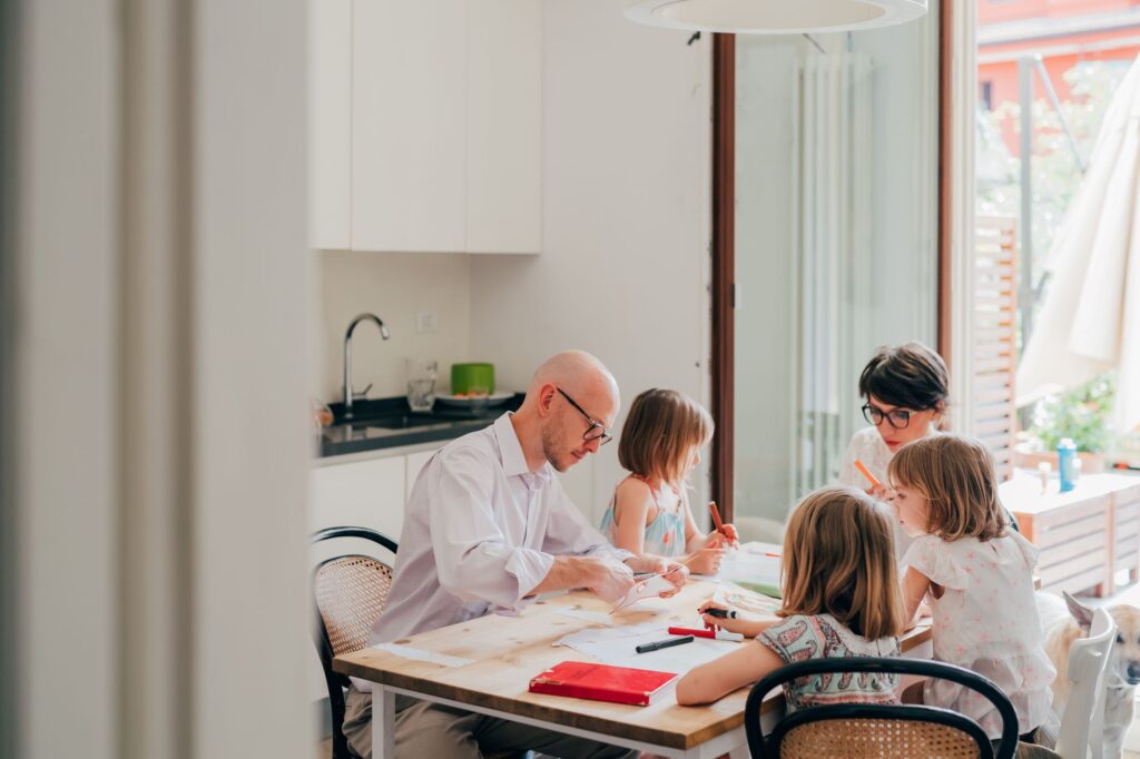 Father doings arts and crafts with his two children on the dining room table.